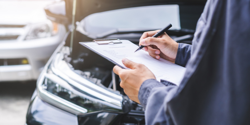 Person inspecting car damage and writing insurance report.