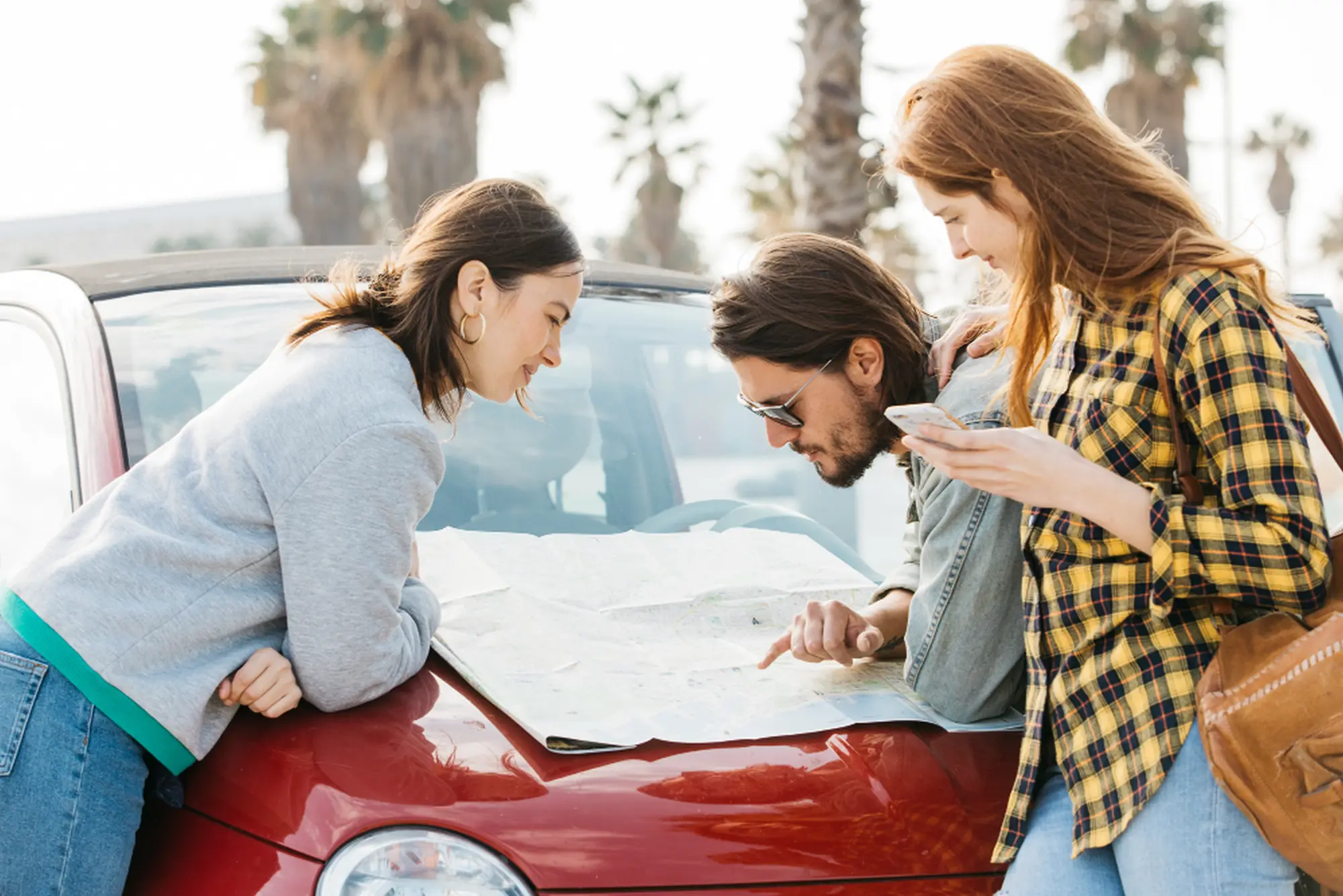 Three people inspecting car damage after an accident on a city street