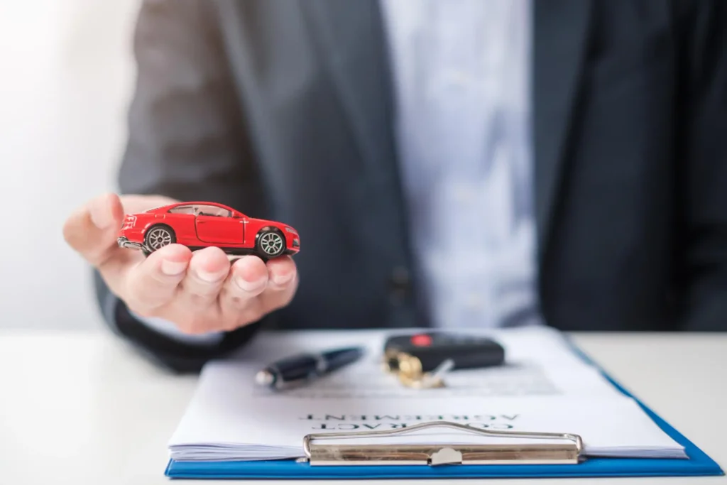 Insurance agent holding car keys above policy documents on desk